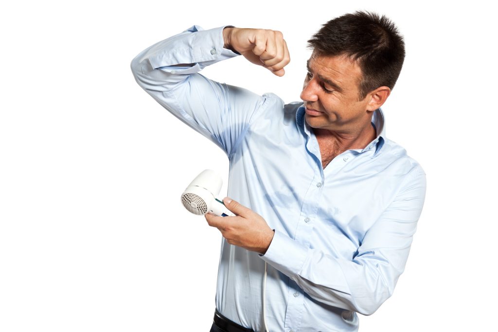 A man pointing a hairdryer at his armpit.