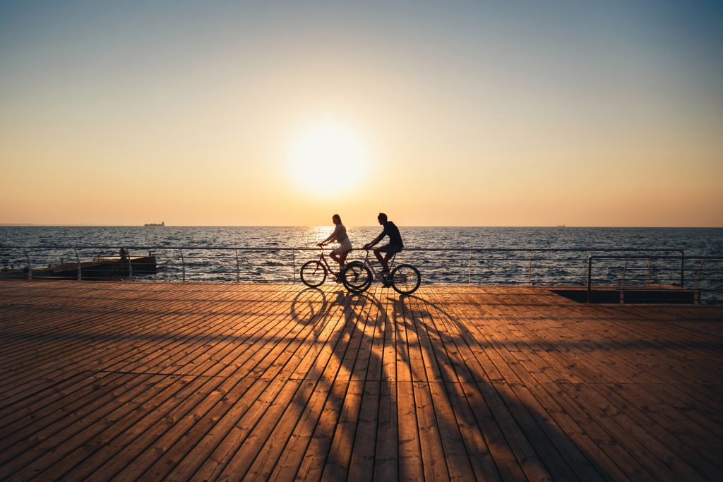 Image of couple cycling together at the beach at sunrise.