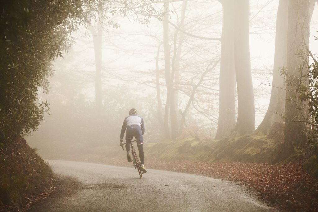 Competitive cyclist riding along foggy road.