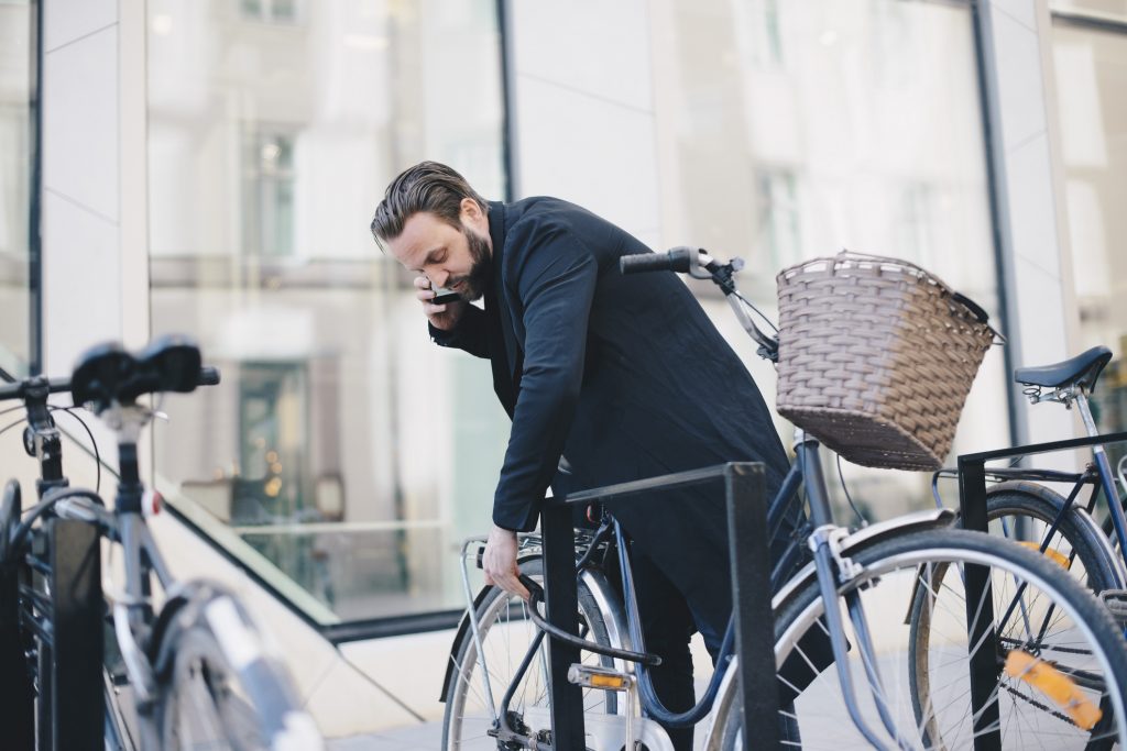 Man talking on mobile phone while unlocking bicycle in city.