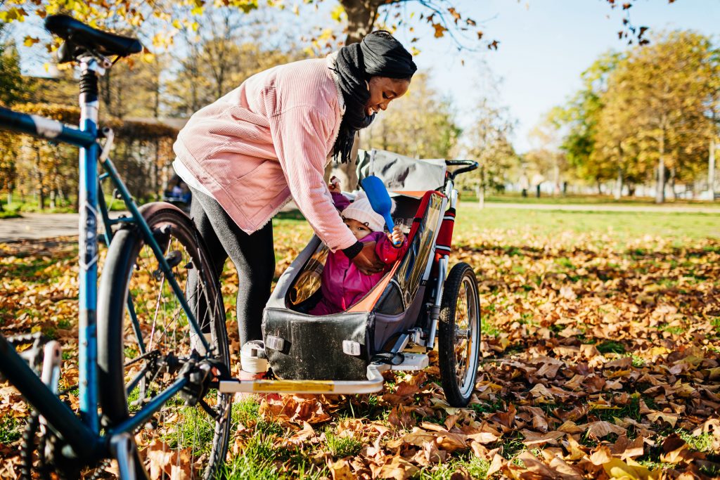 Mom putting toddler into trailer attached to bicycle.