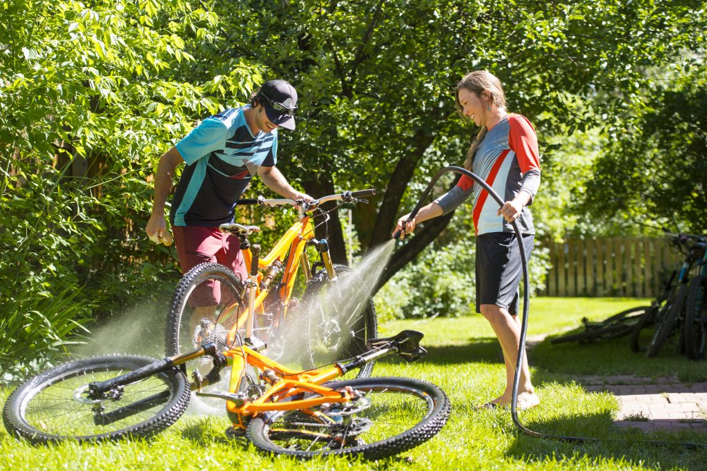 A man and woman washing their mountain bikes in a backyard.