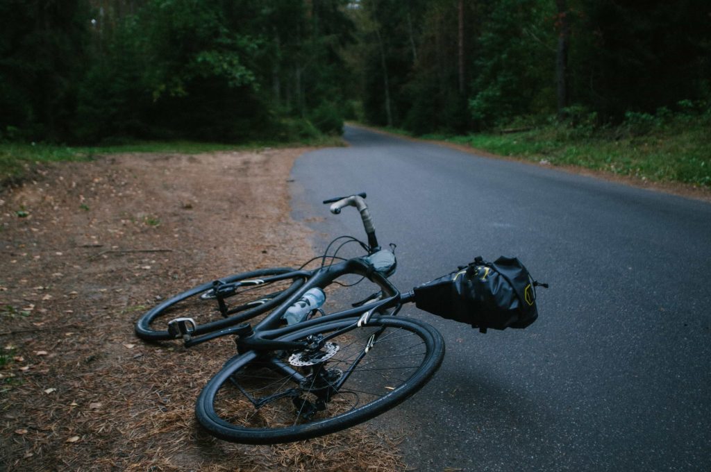 Bike laying on the ground next to open road with trees in the background