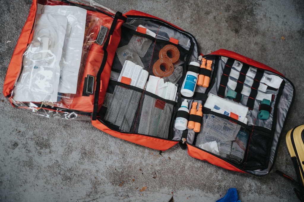 first aid kit laying on the ground, the case is open and orange in colour.