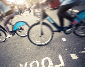 Two cyclists travelling on rented bikes in a busy area.